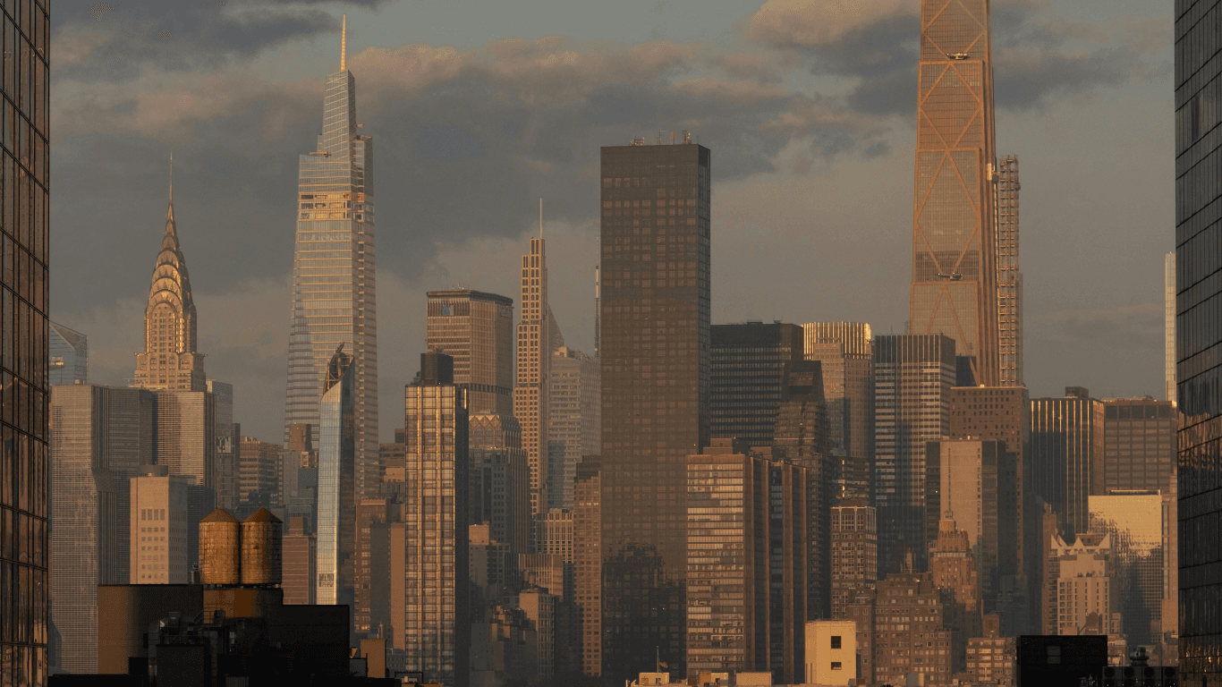 Manhattan skyline at sunset featuring the Chrysler Building and modern skyscrapers under a cloudy sky.