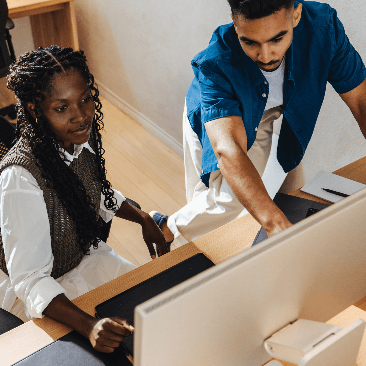 A woman with braids and a man in a blue shirt collaborate at a computer.