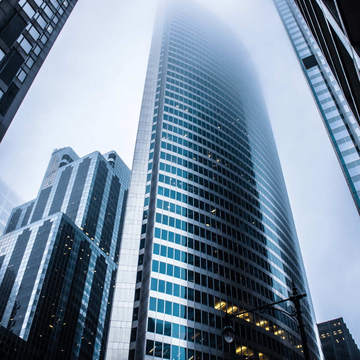 Low-angle view of a curved glass skyscraper with its top disappearing into thick fog.