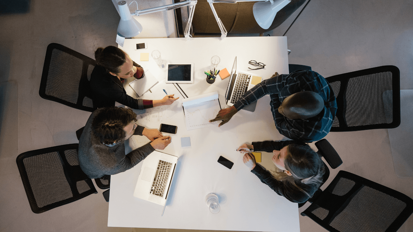 Top-down view of four colleagues collaborating around a white table with laptops and documents.