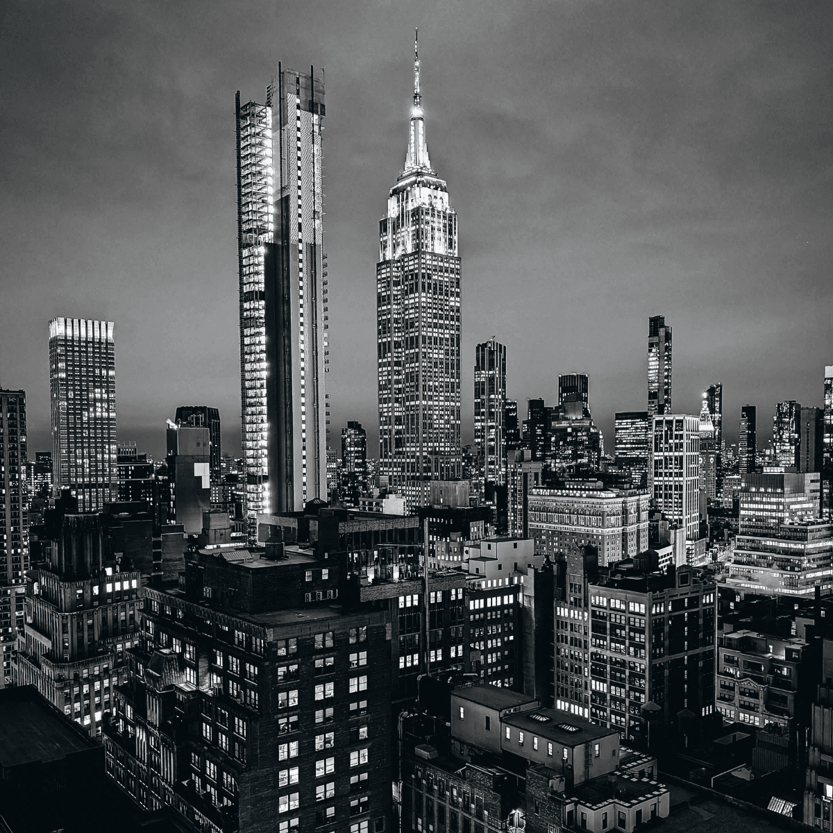 Dramatic black and white night skyline of Manhattan featuring the illuminated Empire State Building.